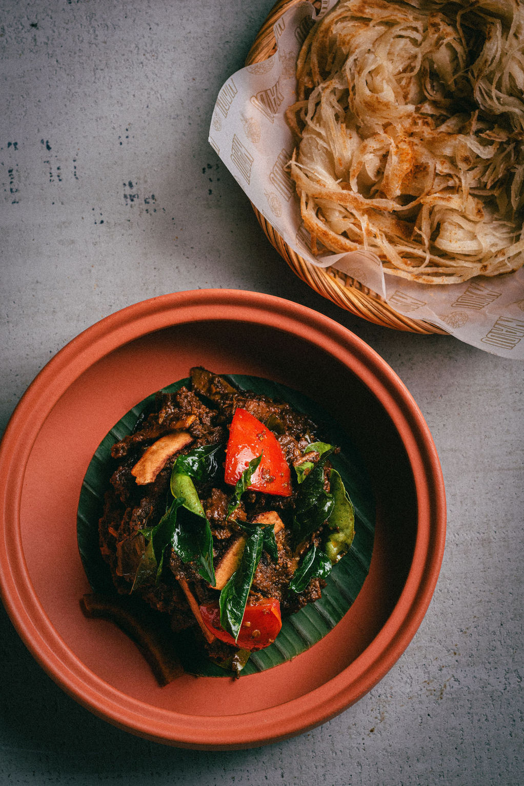 Fried onion strings in a basket with paper lining and a dish of spicy beef stir-fry