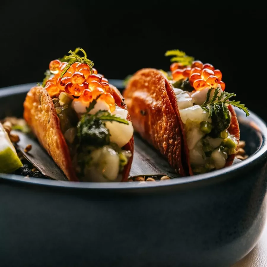 Two tacos filled with seafood, garnished with orange fish eggs and greens
