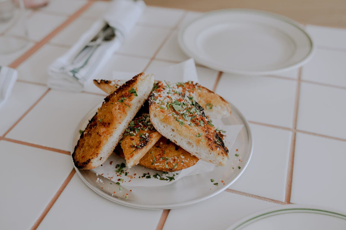 Plate of grilled garlic bread with herbs on a tiled table.