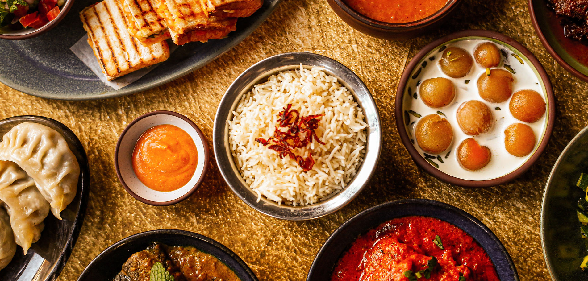 Various Indian dishes on a table, including rice, gulab jamun in milk, and mixed curries.