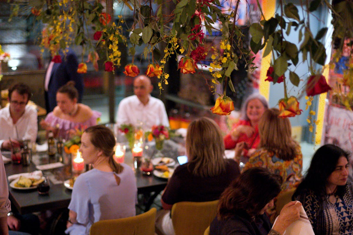 A group of people dining at a restaurant with hanging flowers and candlelit tables.