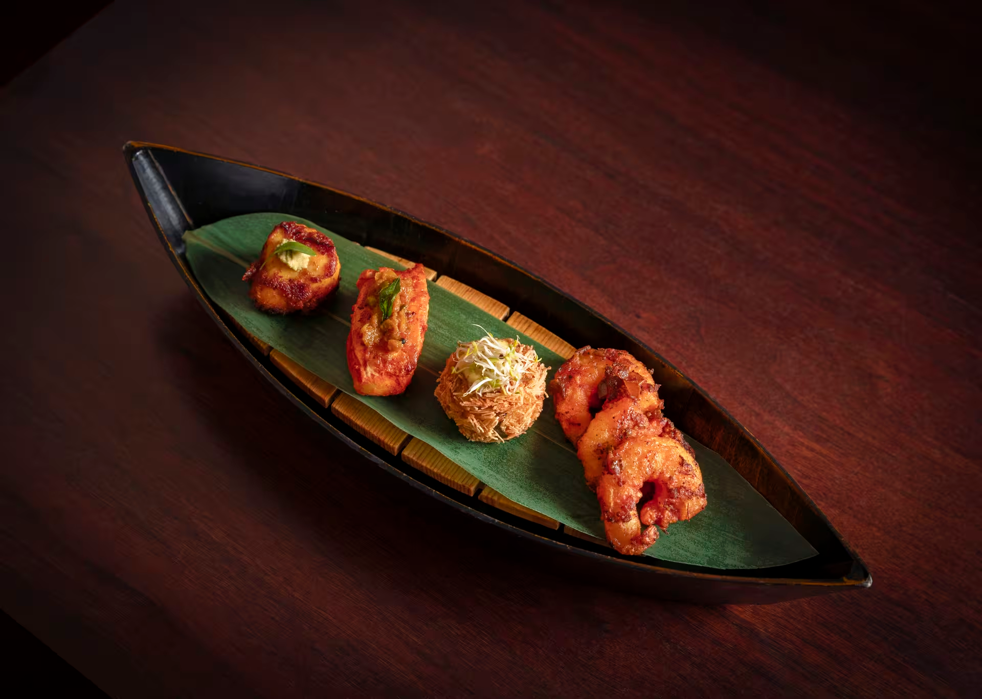 Assorted Indian appetizers served on a long black plate with a green banana leaf.