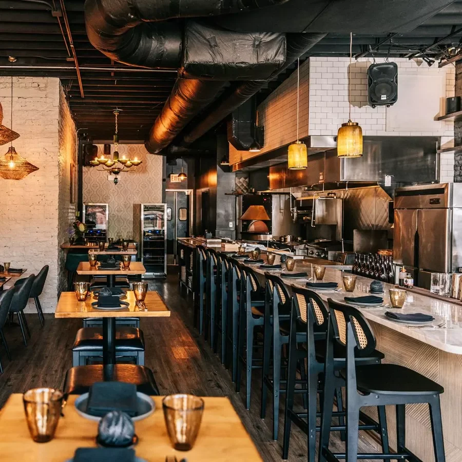 Interior of a modern restaurant showing a bar with wooden tables set with glasses and plates