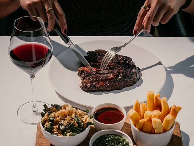 Person cutting a cooked steak with a knife and fork