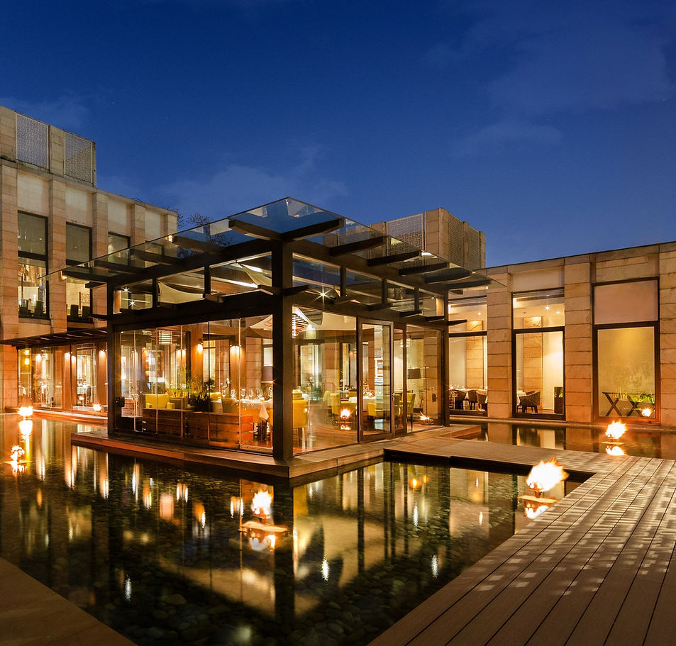 A modern hotel with outdoor pool area at night, illuminated by fire pits.