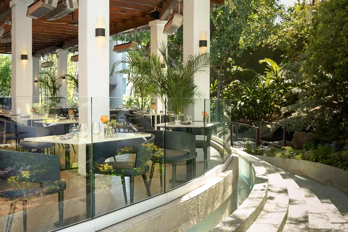 Empty restaurant with white tables, black chairs, and outdoor greenery