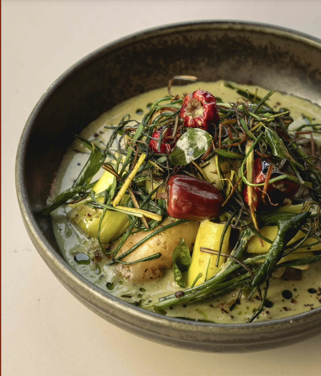 A bowl of stir fried vegetables and red chili peppers in a beautiful green sauce served at Kricket, London.