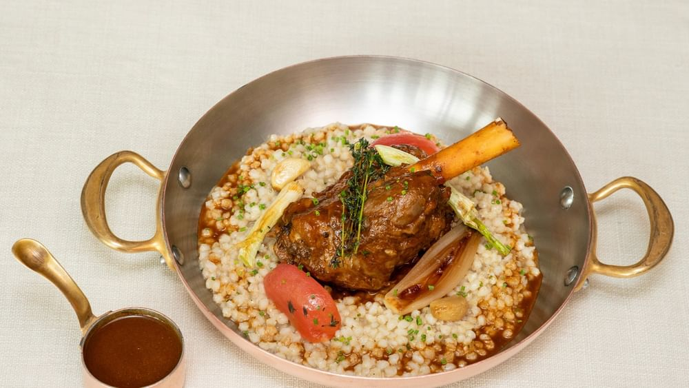 A plate of lamb shank served over pearl millet porridge with vegetables and gravy