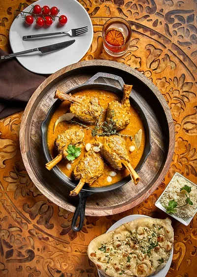 A top-down view of a traditional Indian meal featuring a pot of lamb curry