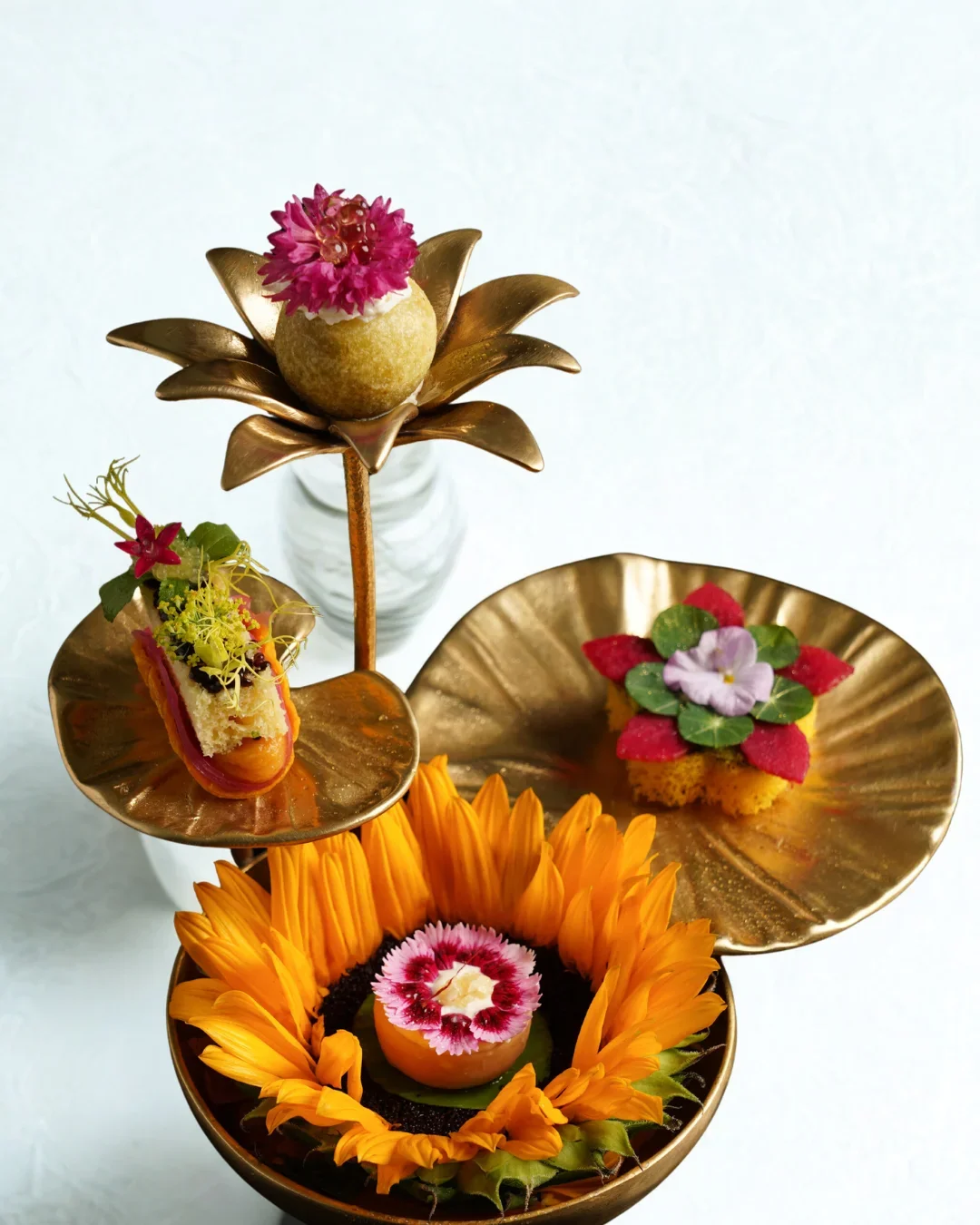 Artfully arranged gourmet desserts and flowers on golden plates and stands.