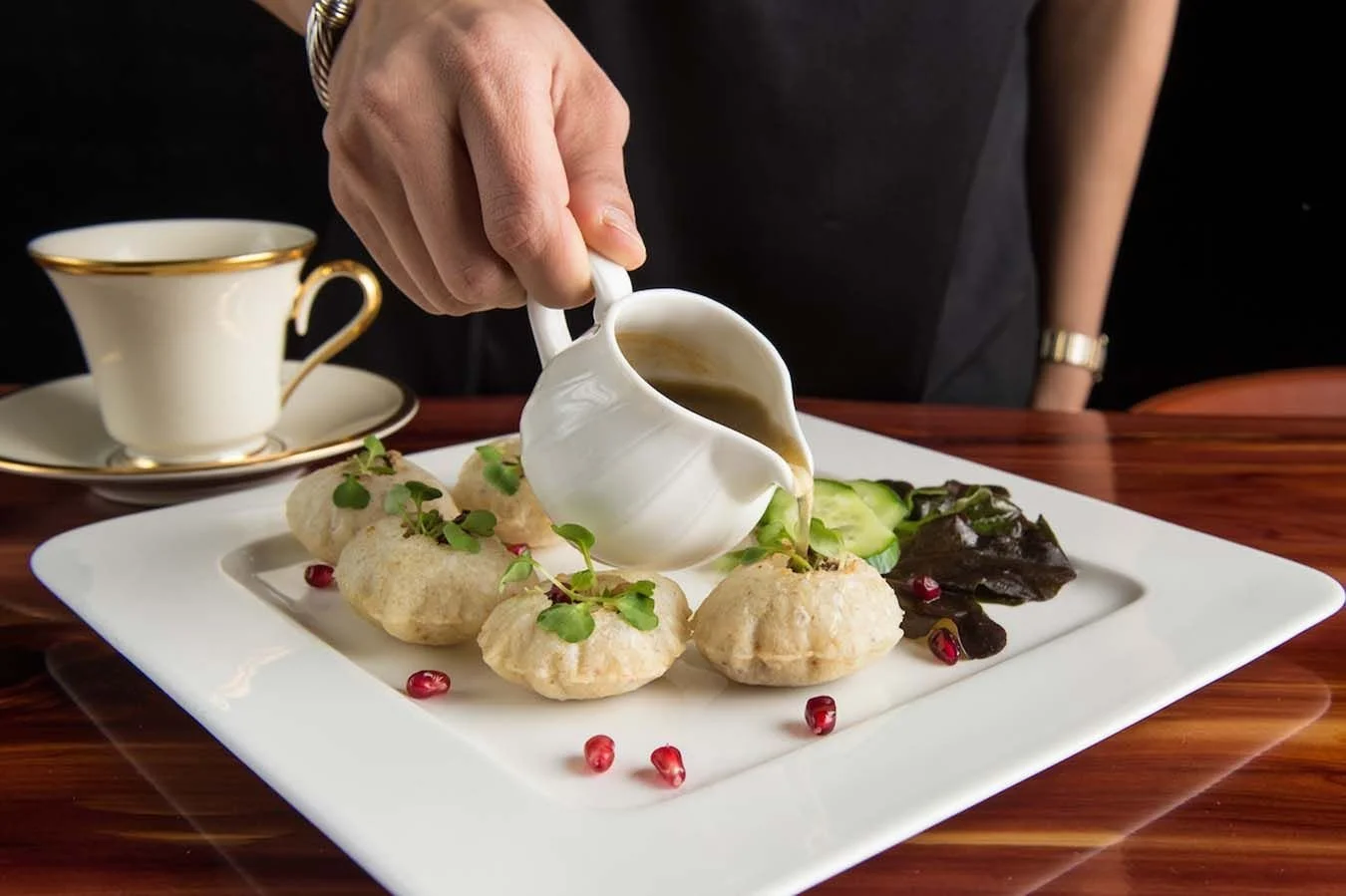 A person pouring sauce over a plate of food with dumplings