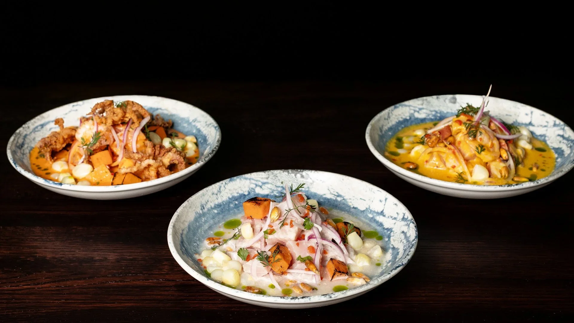 Four bowls of colorful Asian cuisine dishes on a dark wooden table.