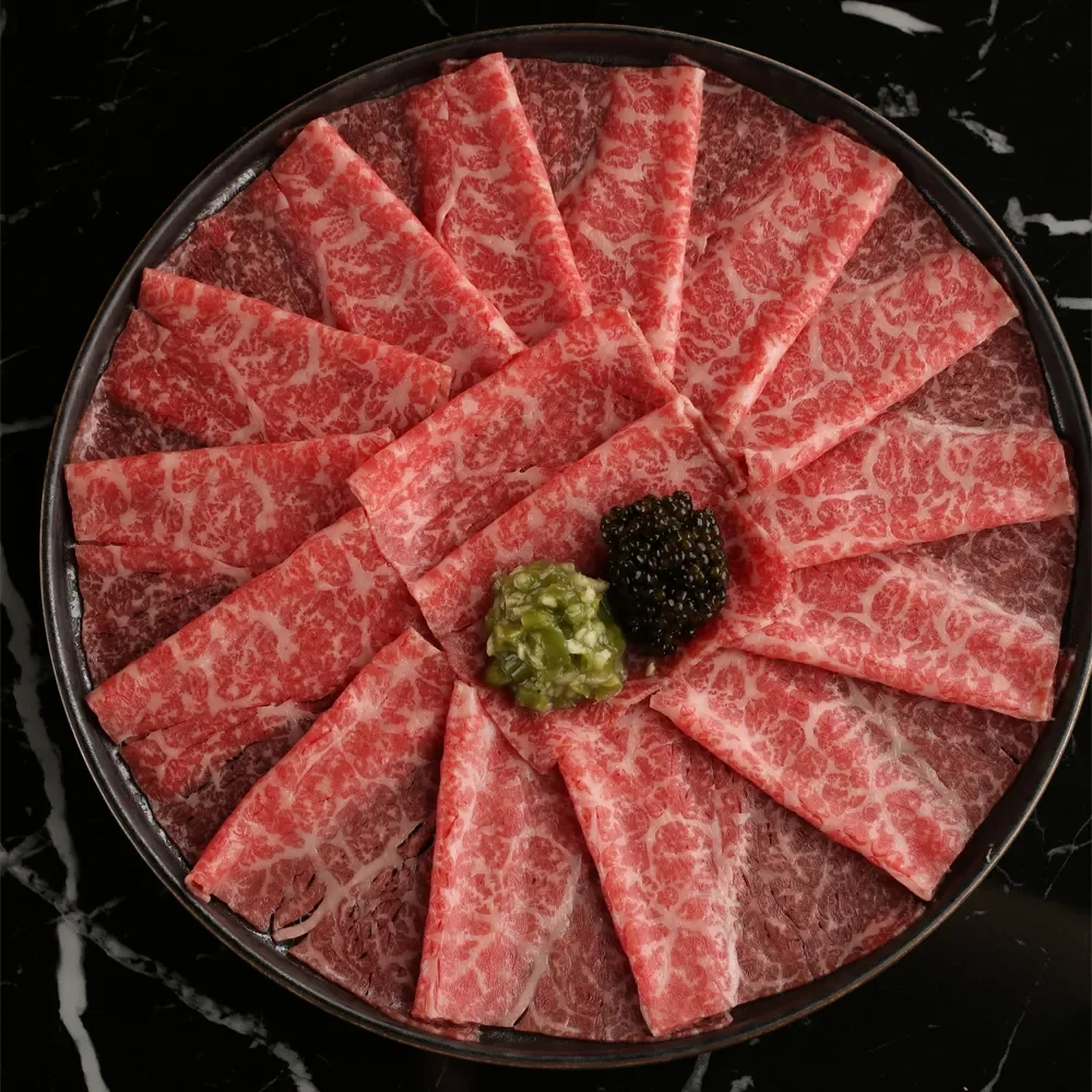 Thinly sliced marbled beef arranged in a circular pattern on a black marble surface