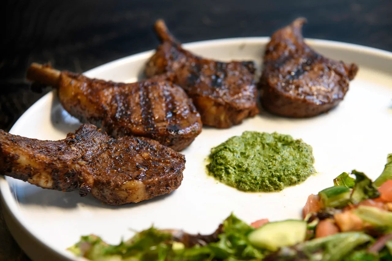 Plate with grilled lamb chops, green chutney, and salad.