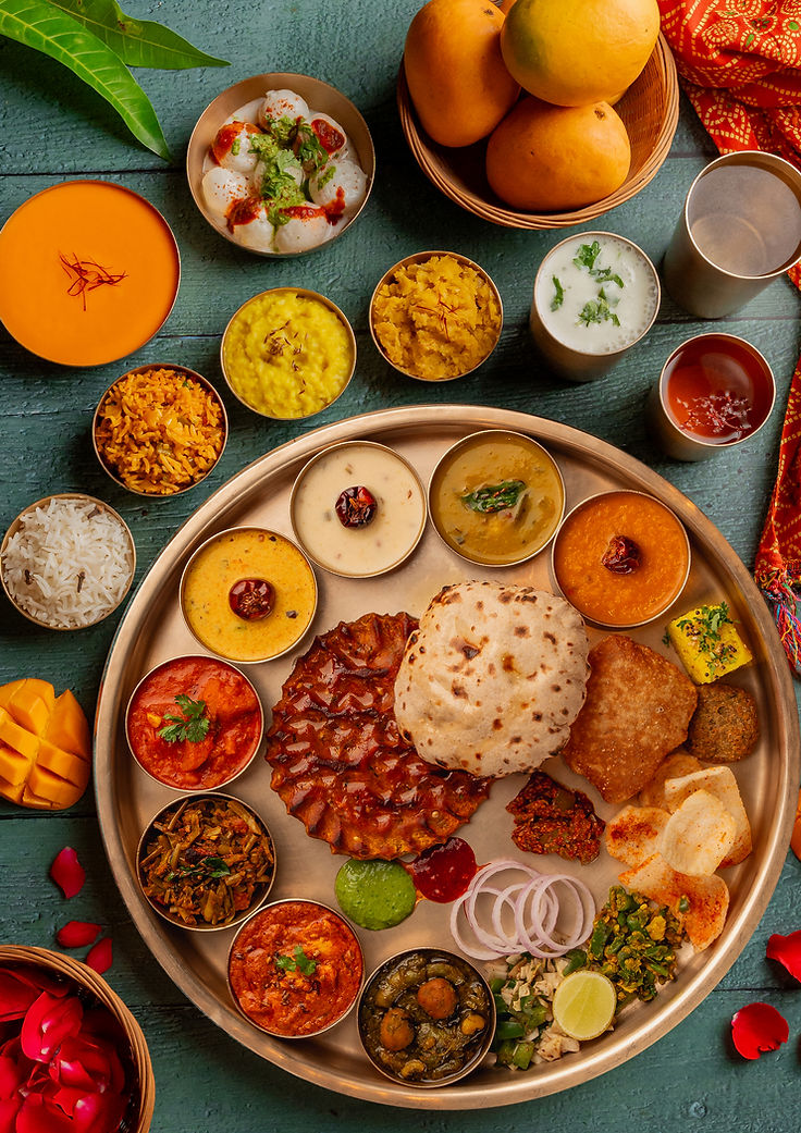 Traditional Indian thali with various curries, rice, bread, fruits, and condiments
