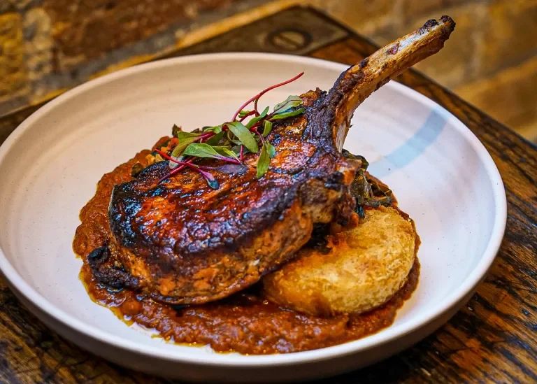 Lamb chop with a tomato-based sauce, garnished with microgreens
