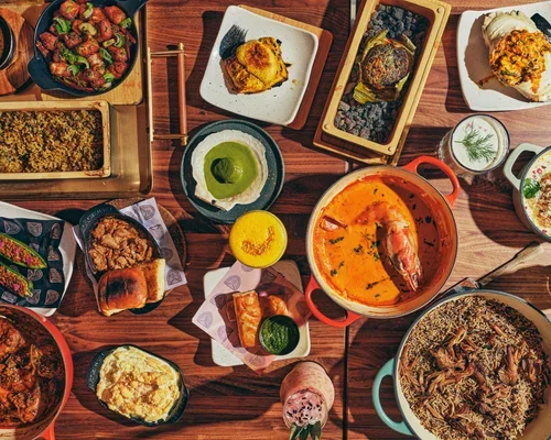 A variety of dishes including soups, curries, bread, and desserts arranged on a wooden table.