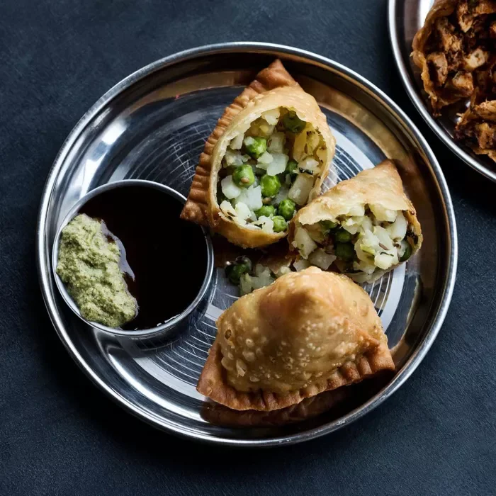 Two vegetable-filled samosas on a metal plate with green chutney.