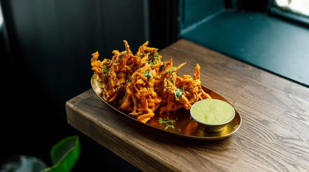 Plate of crispy vegetable fritters with green dipping sauce on a wooden table.