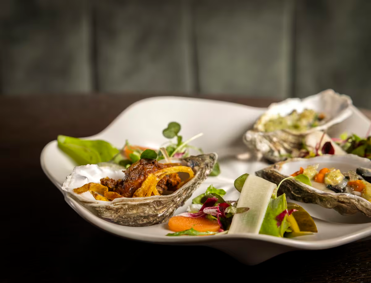 Oysters served on a white plate with garnishes and salad greens.