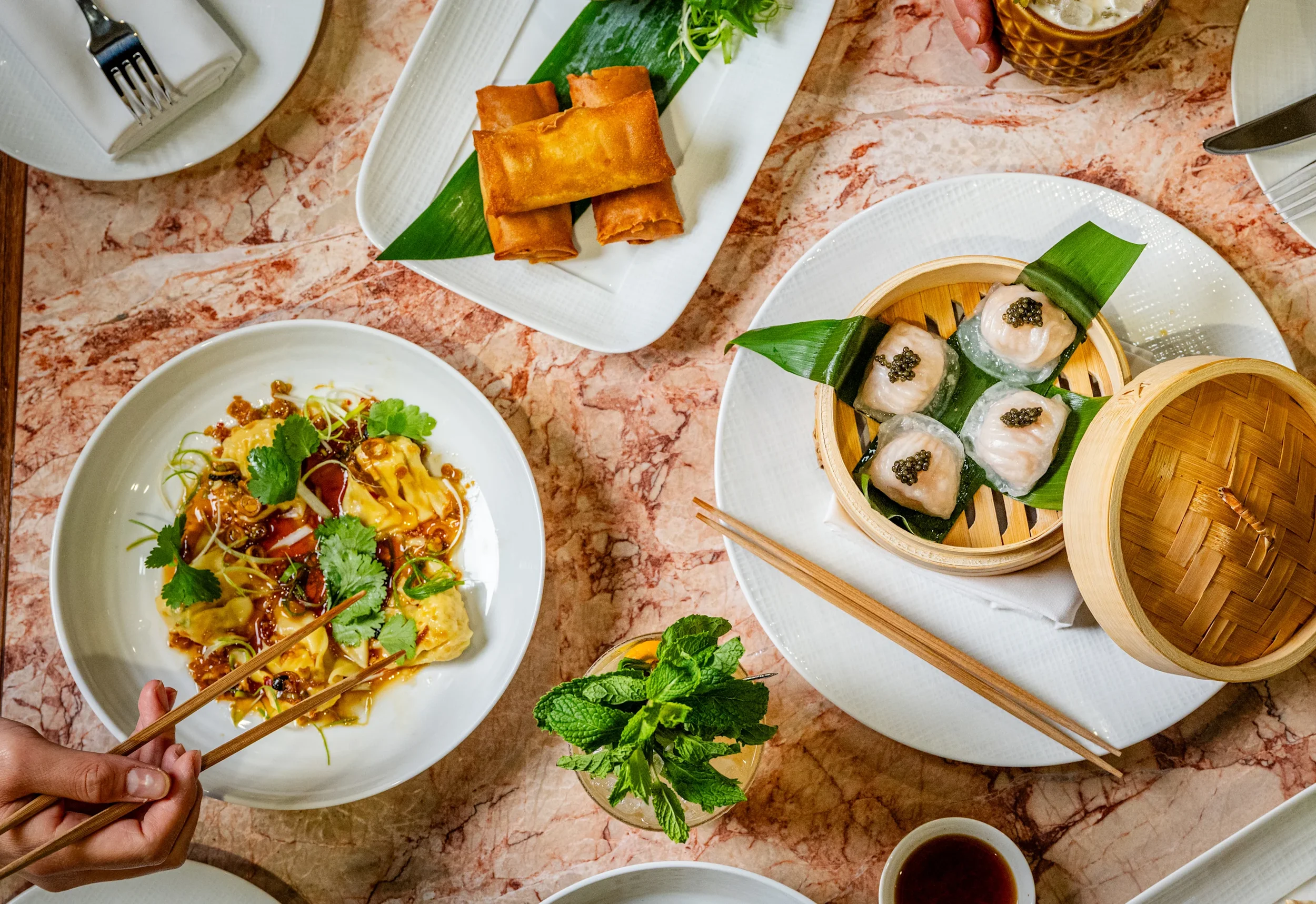 A variety of Asian dishes on a marble table, including spring rolls on a rectangular plate.