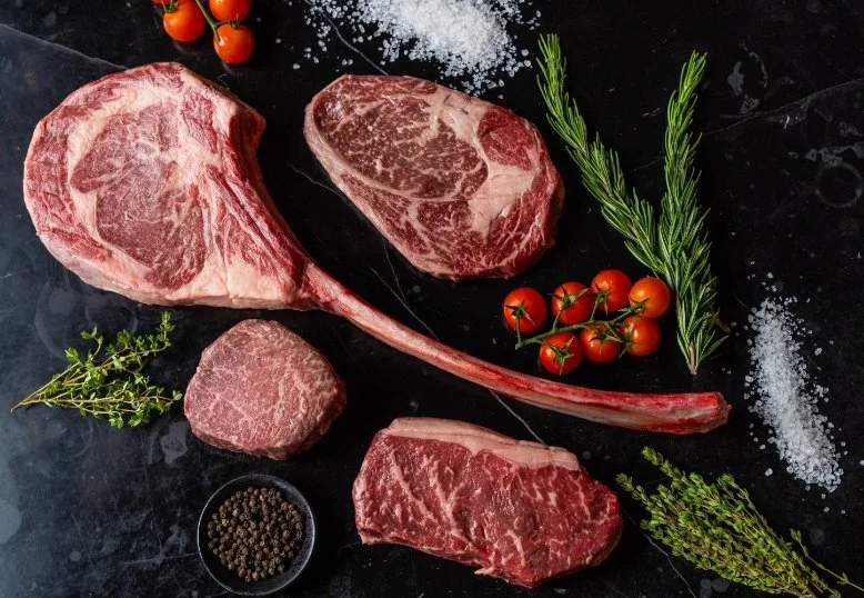 Raw beef steaks and a tomahawk chop on a black surface