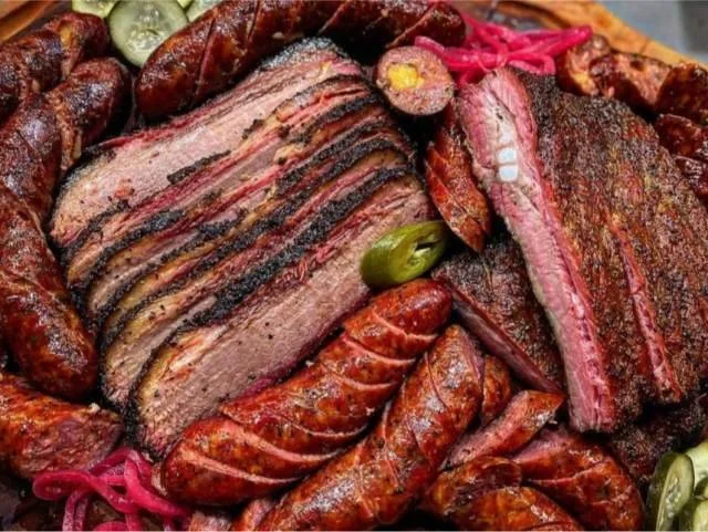 Assorted grilled meats including sliced brisket, sausages, and ribs