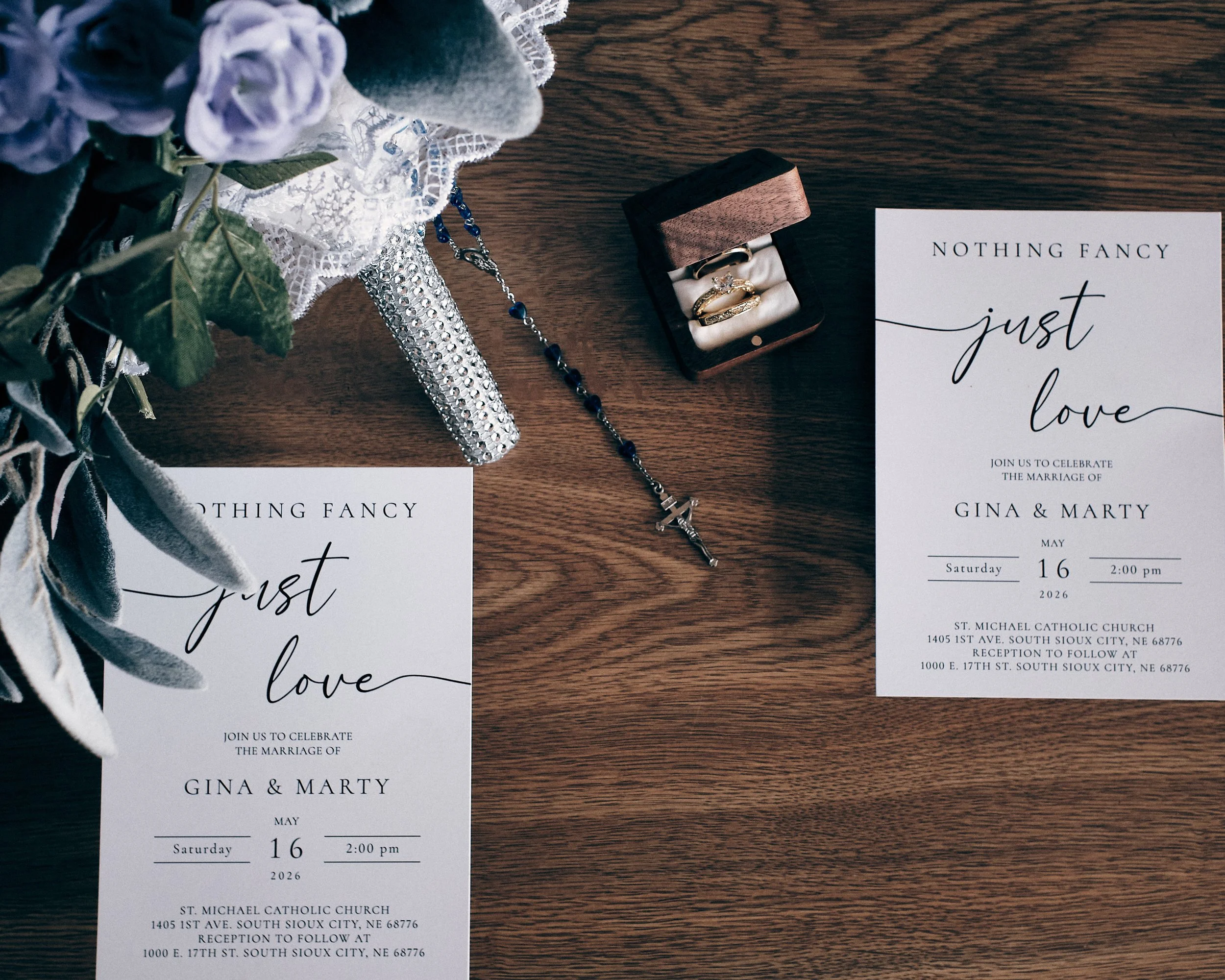 Wedding invitation, ring box with rings, jewelry, flowers, and a decorative item on a wooden surface.