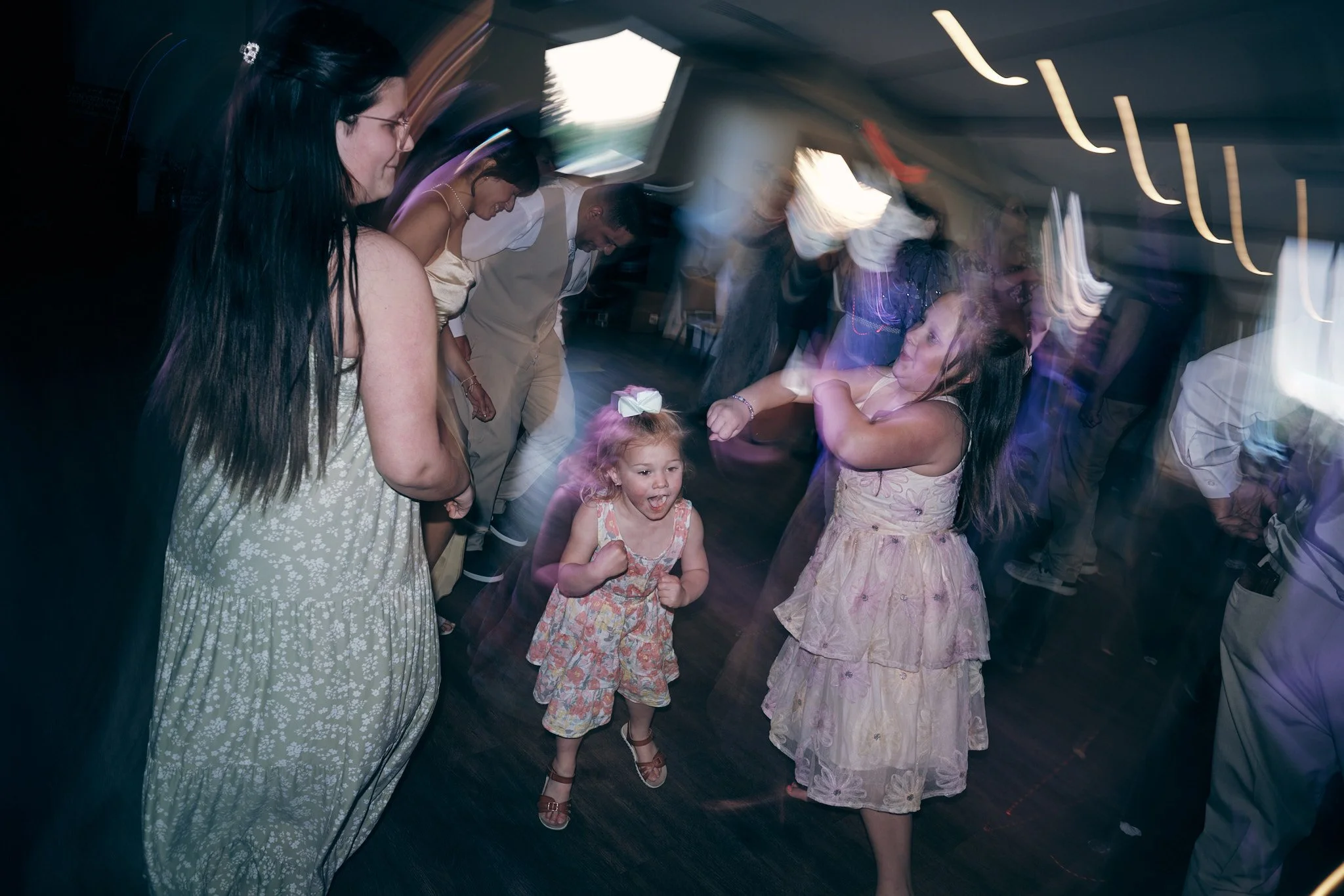 People dancing at a party, including young girls and women, with motion blur and colorful lighting.