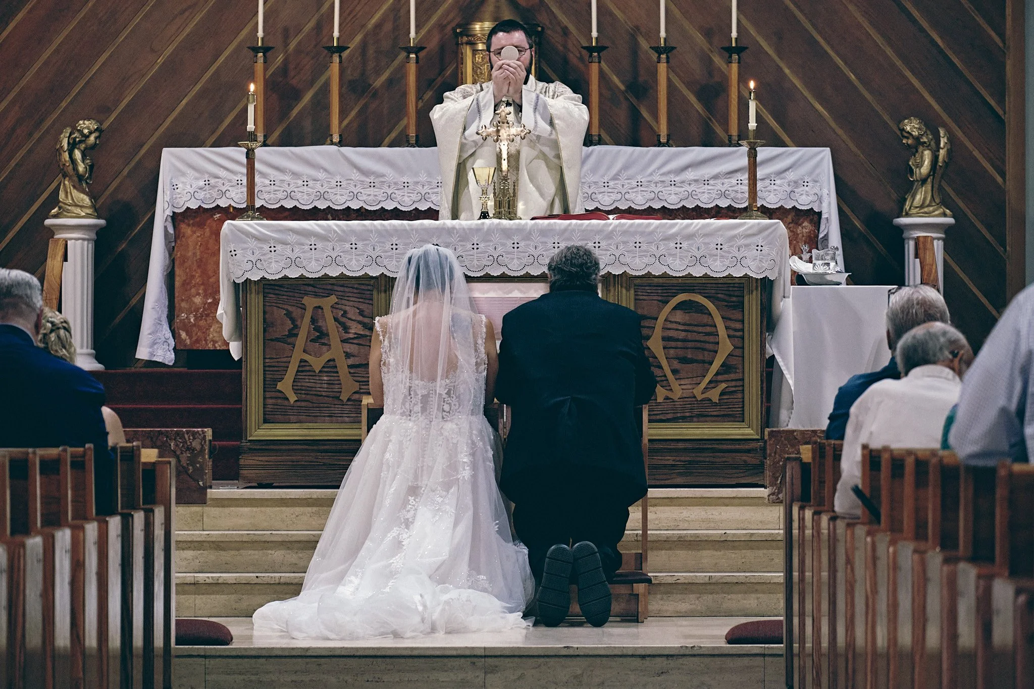A priest conducting a wedding ceremony in a church with a bride and groom kneeling at the altar.