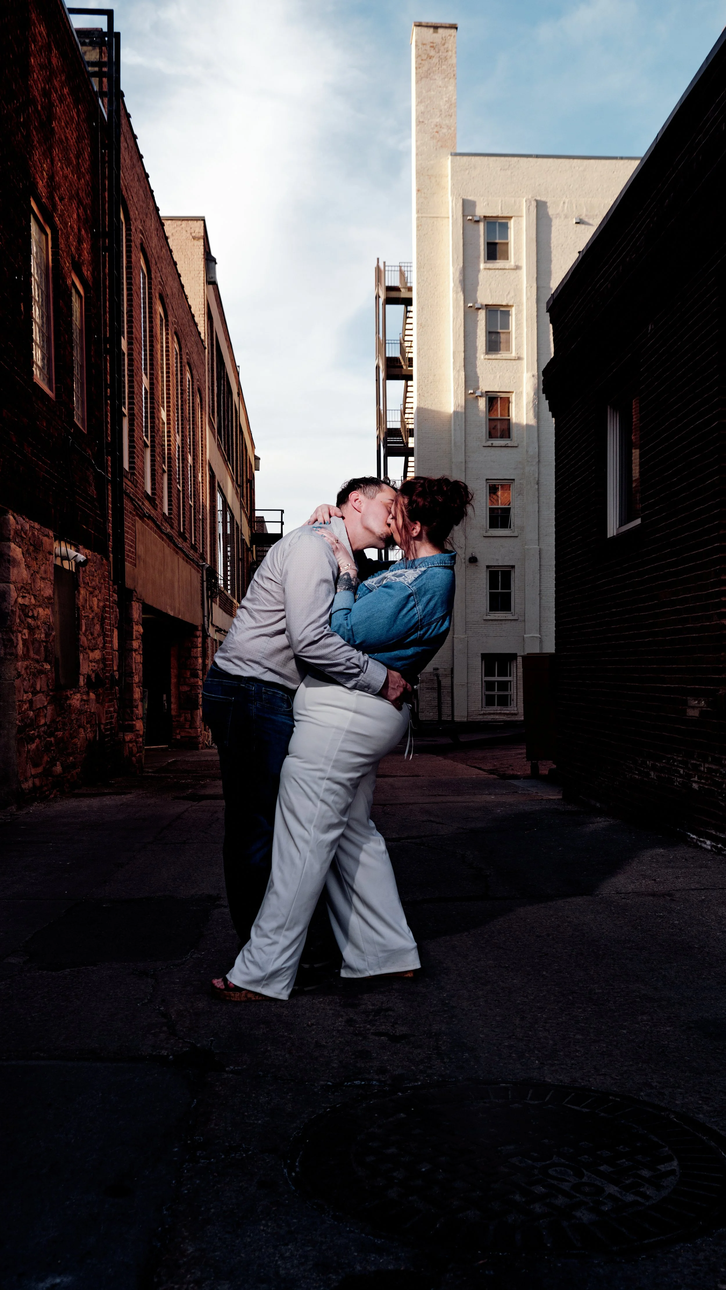 A couple kissing in a narrow alleyway with tall buildings on either side.