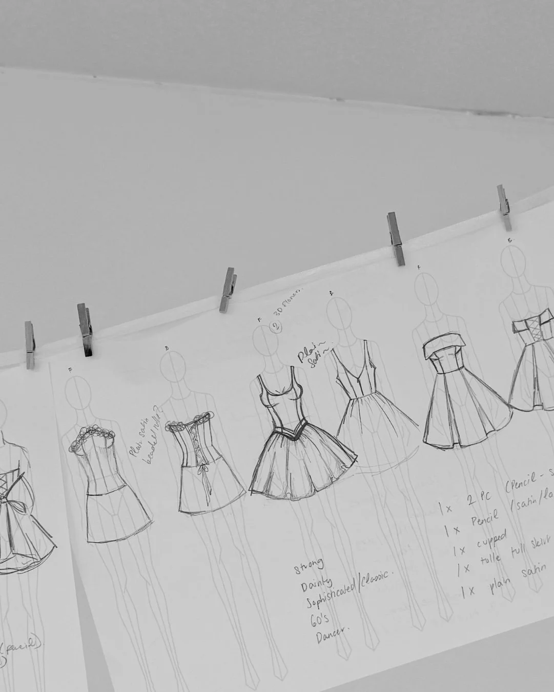 Sketches of different dress designs pinned to a board with clips.