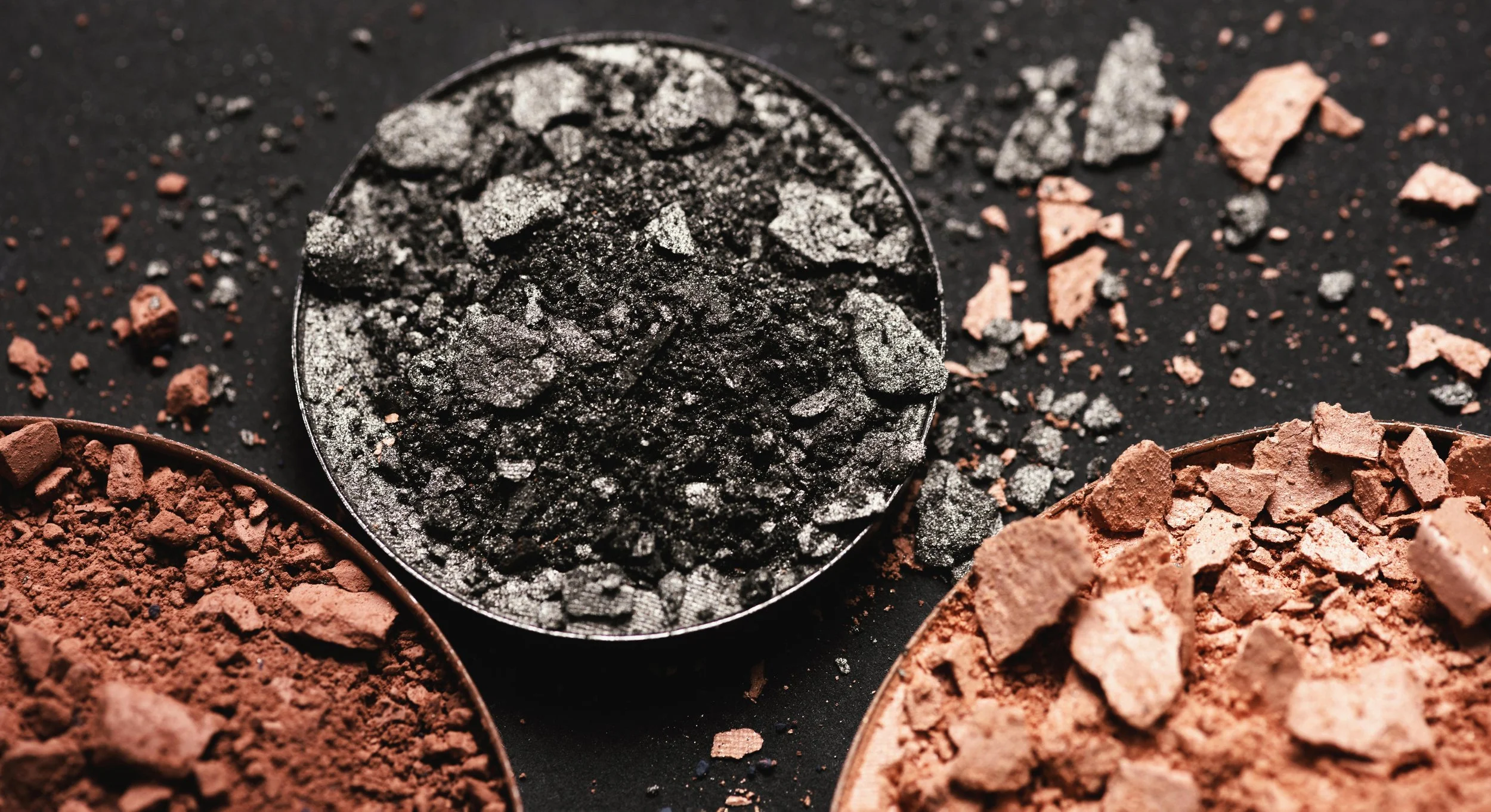 Close-up of black and pink powdered makeup minerals on a black background.
