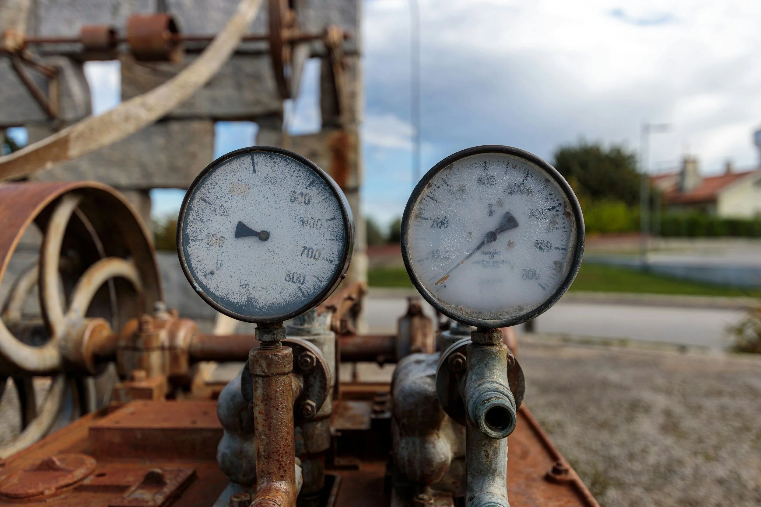 Close-up of two rusted pressure gauges, one showing around 600 psi and the other around 200 psi, on an old, rusty industrial machine outdoors.