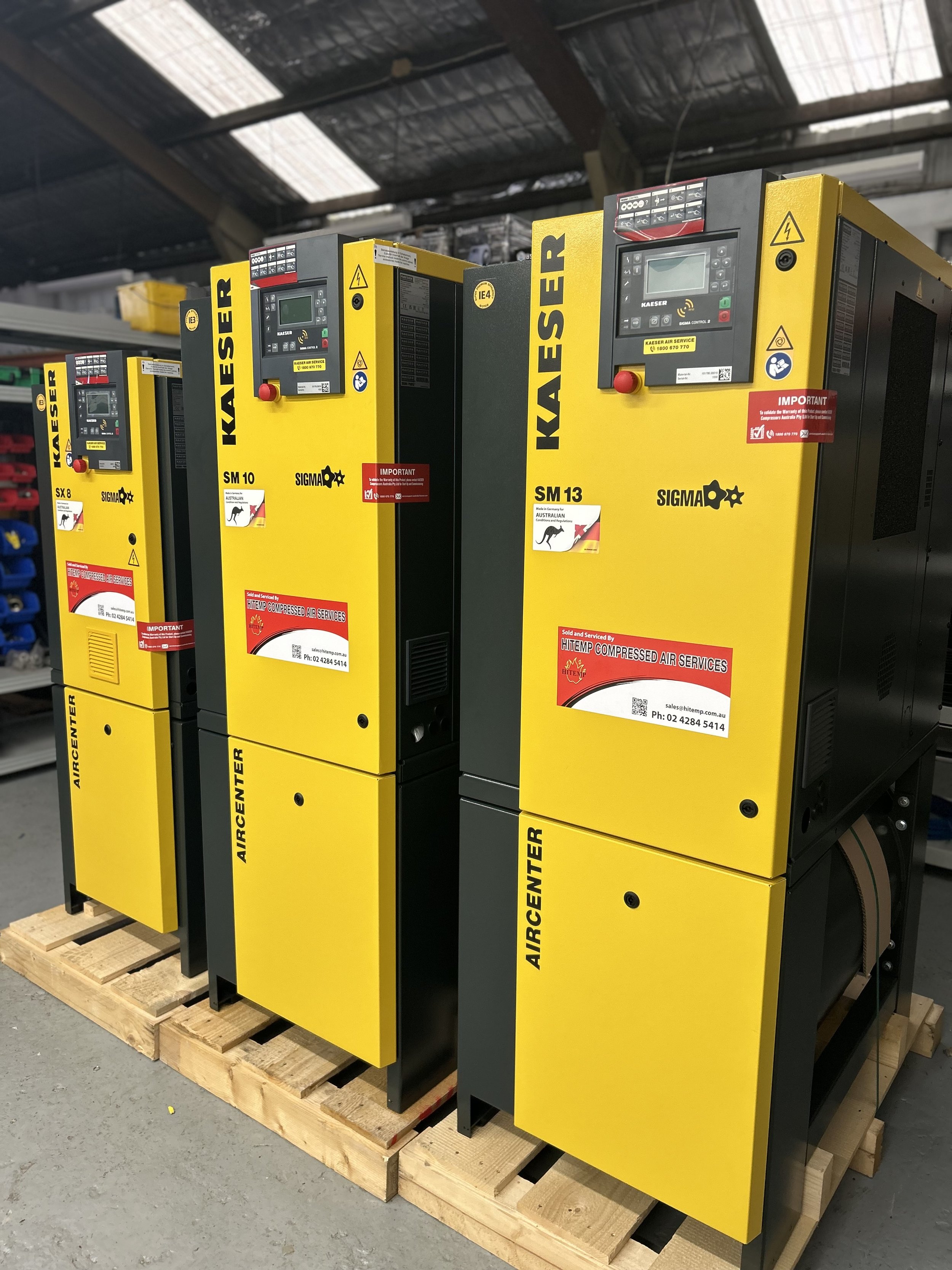 Three yellow and black industrial air compressors on a wooden pallet in a warehouse.