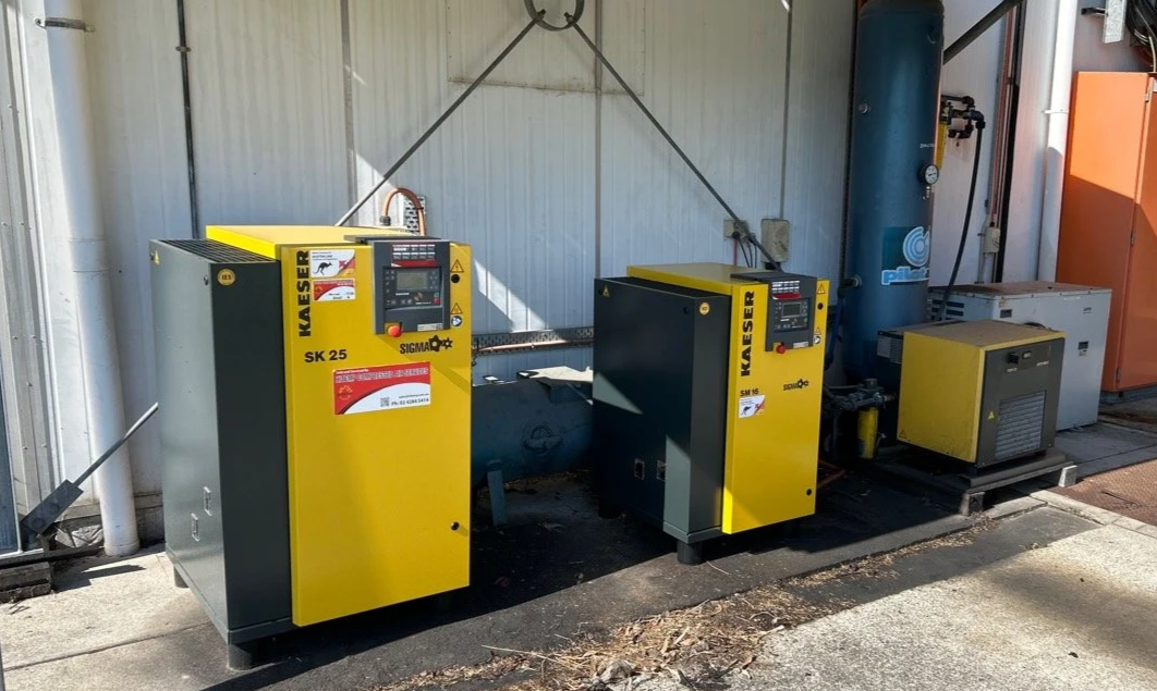 Industrial air compressers on a concrete floor in a utility room.