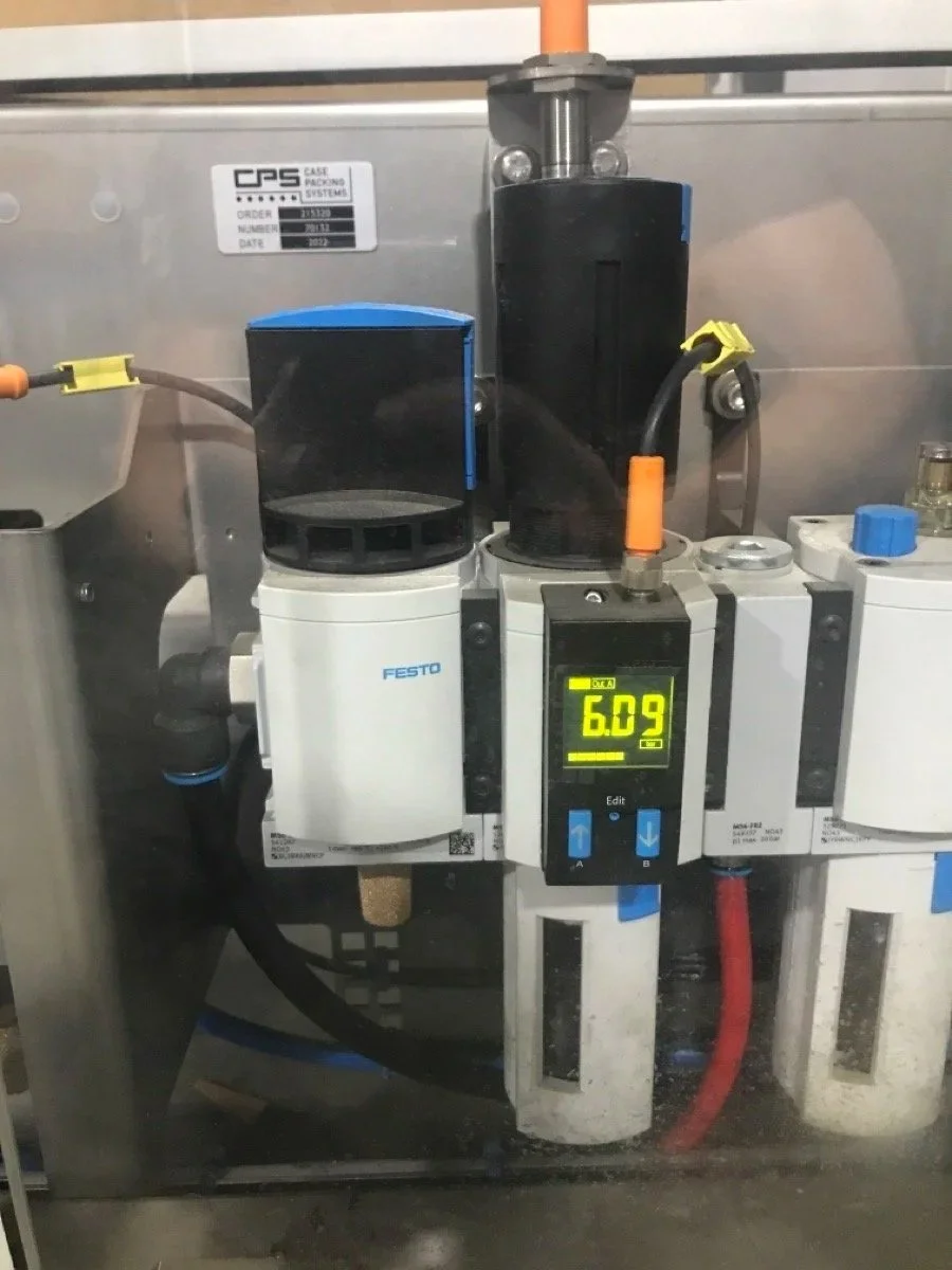 Close-up of industrial machinery with electronic display showing 6.09, connected to pipes and fittings, with labels and wires, used in manufacturing or processing.