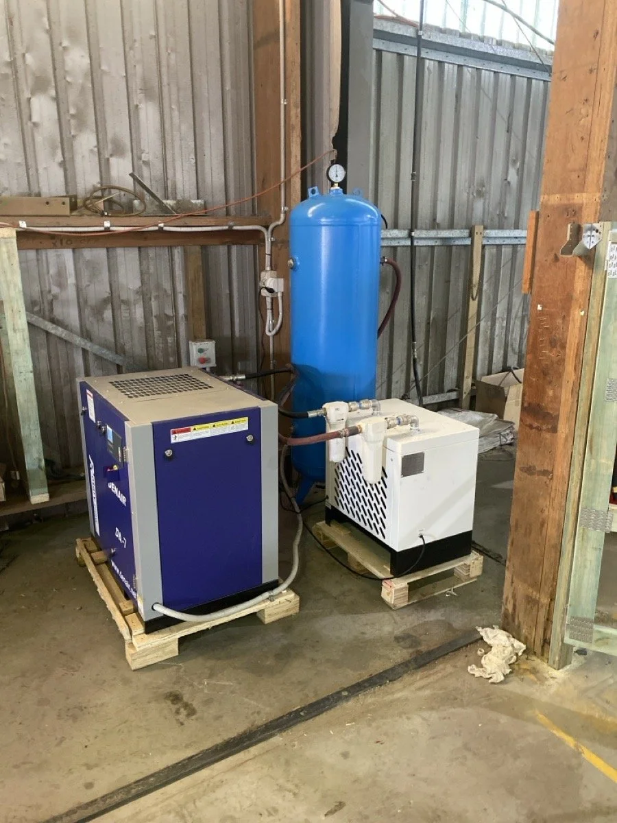 Industrial air compressor system with a blue tank, white compressor, and blue and white control units in a factory setting.