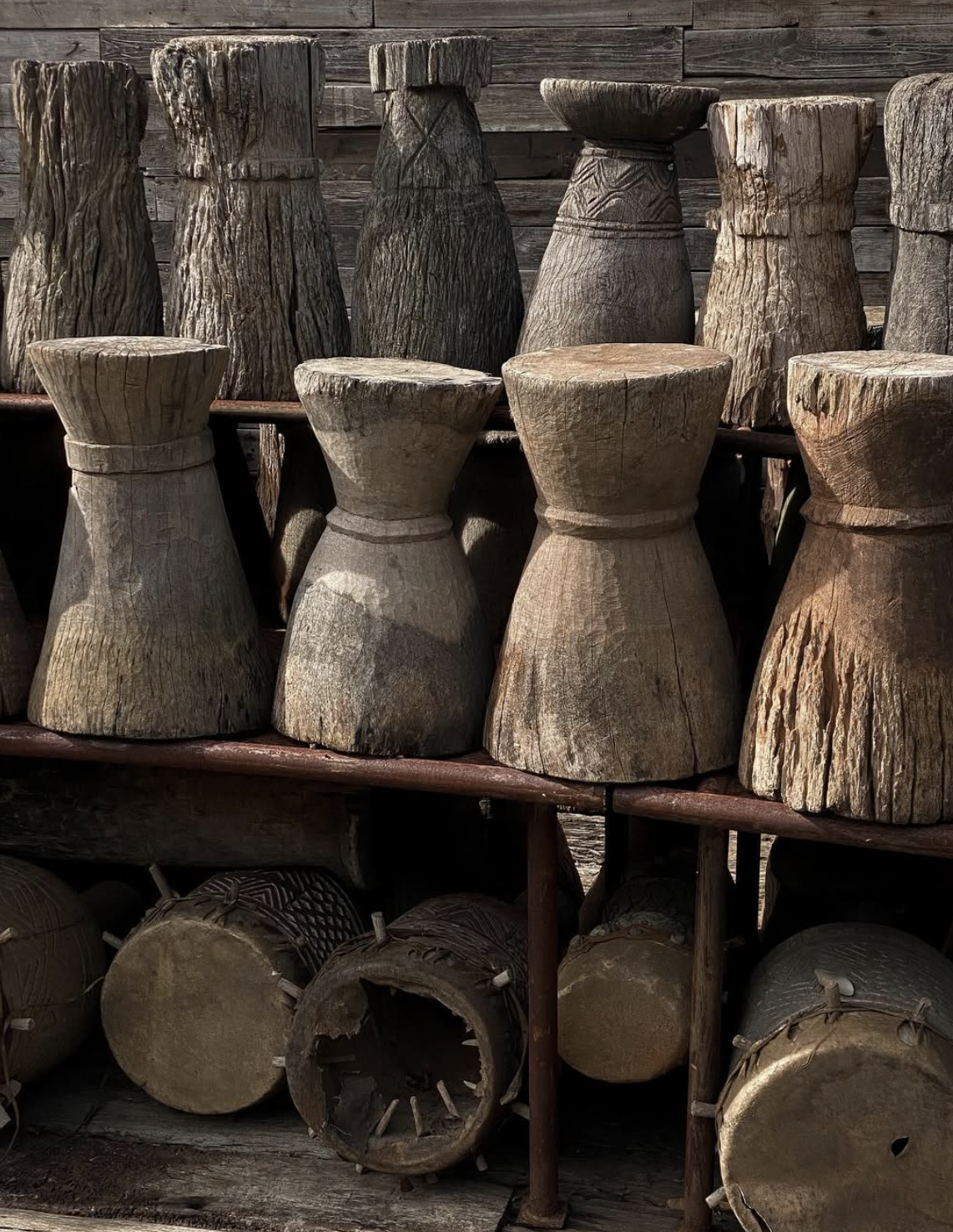A display of carved wooden objects, possibly stools or drums, arranged on shelves outdoors.