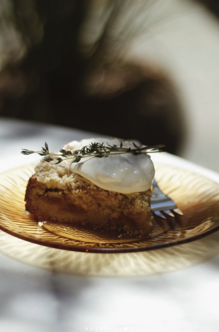 Slice of cake with cream, garnished with a sprig of thyme on a yellow plate