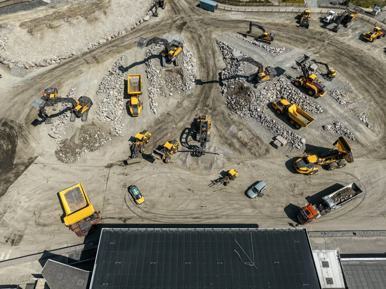 Aerial view of a construction site with multiple yellow and black excavators and dump trucks moving dirt and rocks.