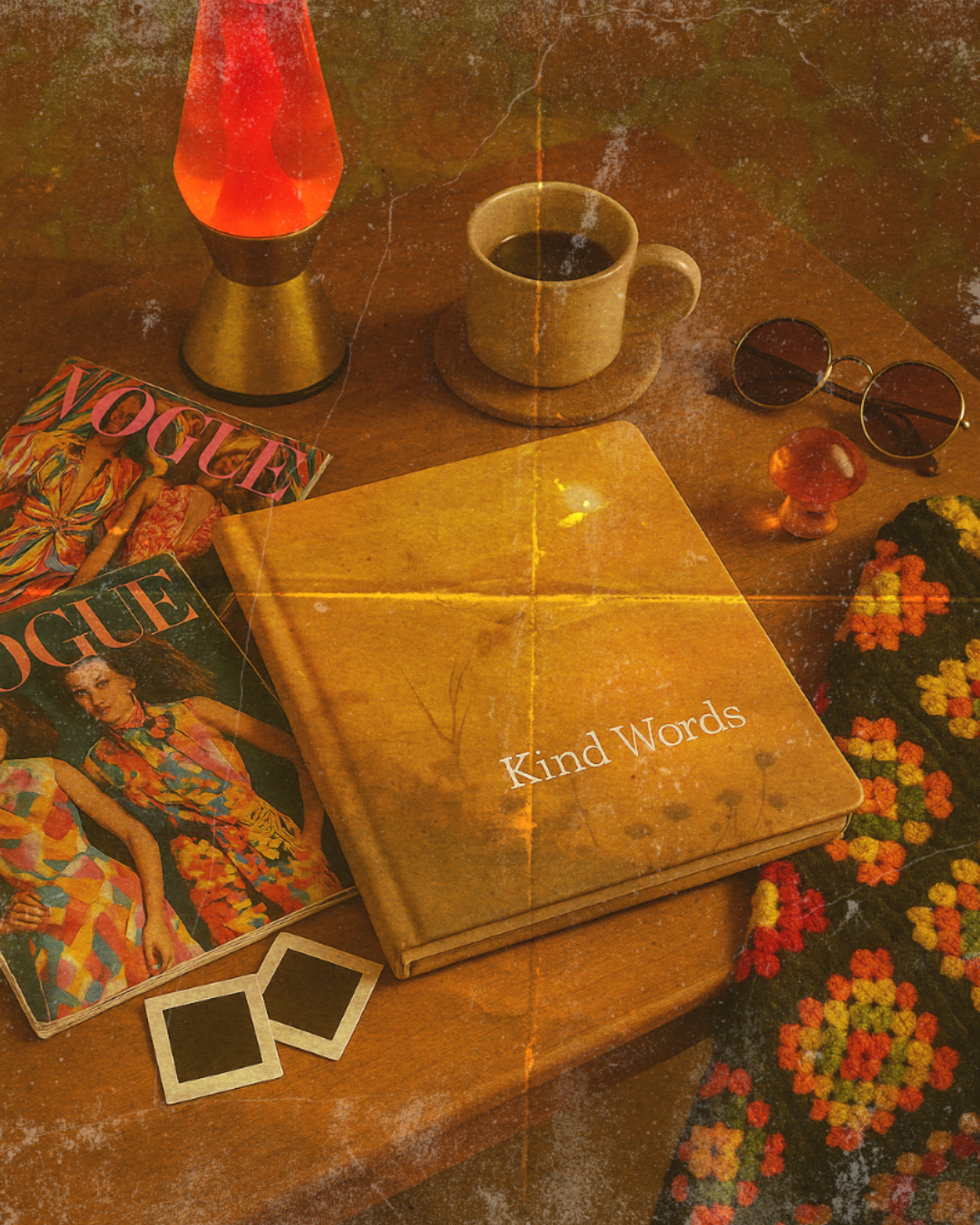 A wooden table with a vintage aesthetic holding a book titled 'Kind Words', two Vogue magazines, a pair of round sunglasses, a ceramic cup of coffee on a small saucer, a lava lamp, a colorful crocheted item, a mushroom-shaped object, and a printed fabric with orange, yellow, and green floral patterns.