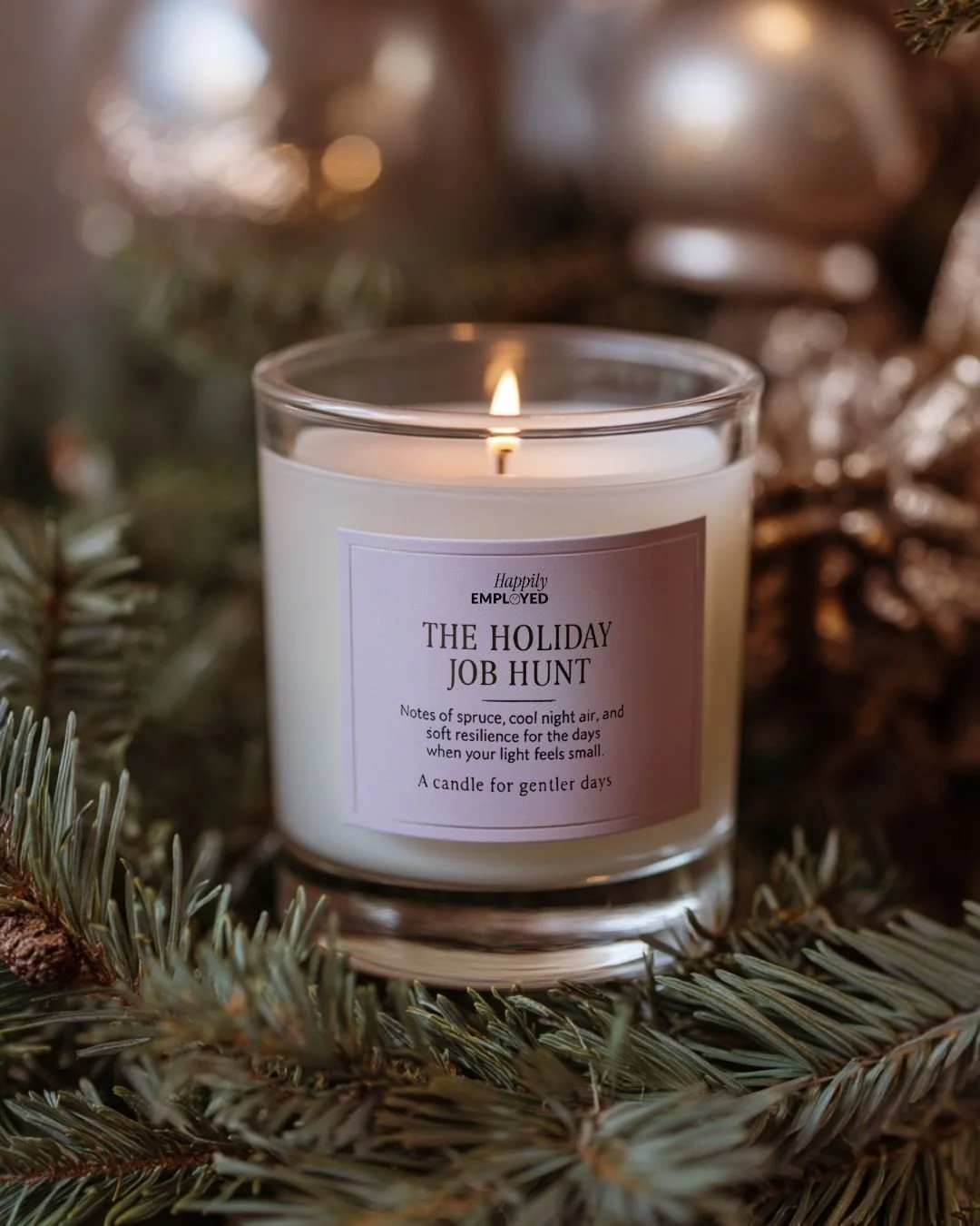 A white candle labeled "The Holiday Job Hunt" with a lit flame, surrounded by pine branches and Christmas decorations.