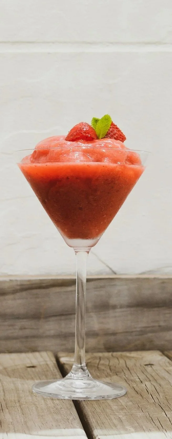 A glass of strawberry sorbet garnished with a strawberry and a mint leaf.
