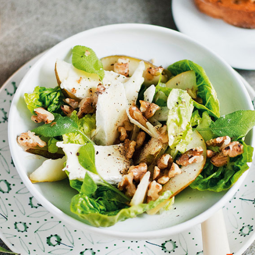 Insalata mista con rucola, pere, noci e formaggio parmigiano in una ciotola bianca.