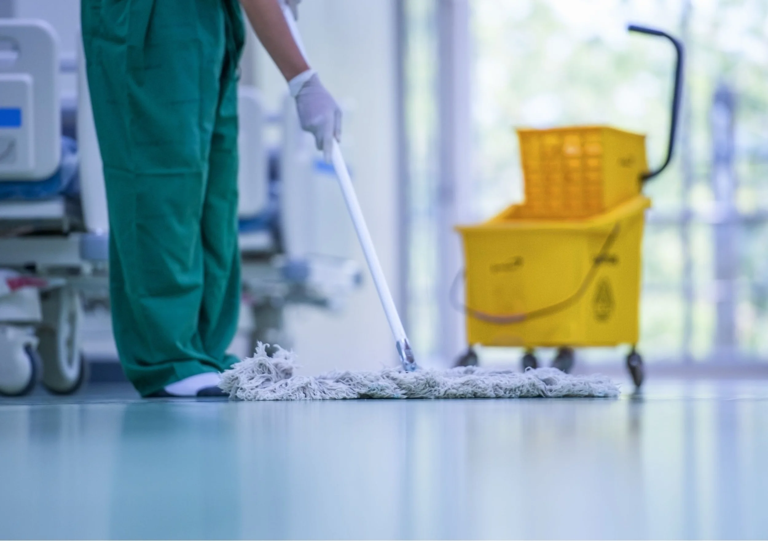 A cleaner cleans a commercial floor, with a yellow cleaning cart in the background.