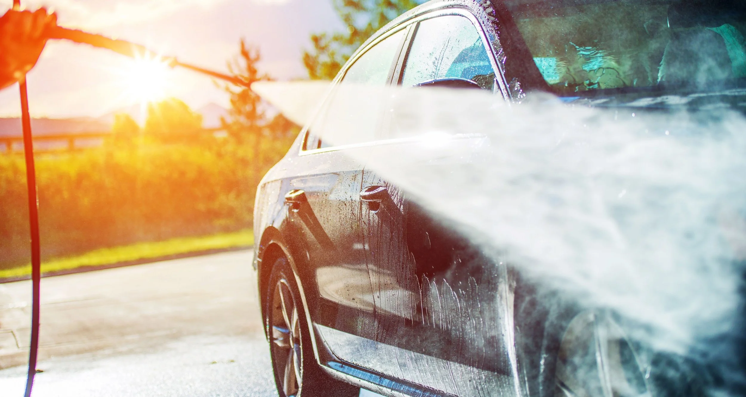 Black car being washed outdoors with a hose on a sunny day