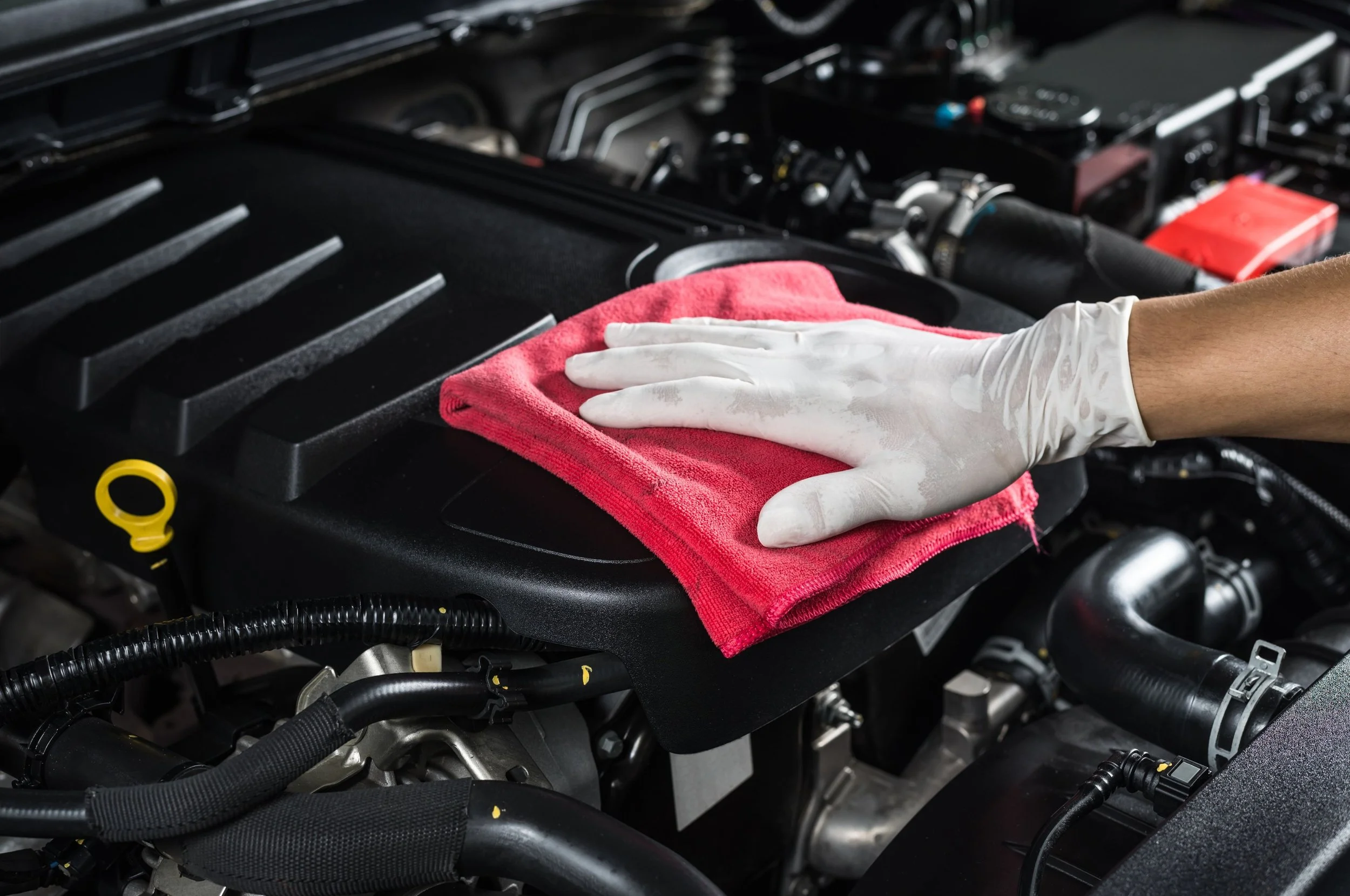 Detailing expert wearing gloves cleaning a car engine with a red cloth.