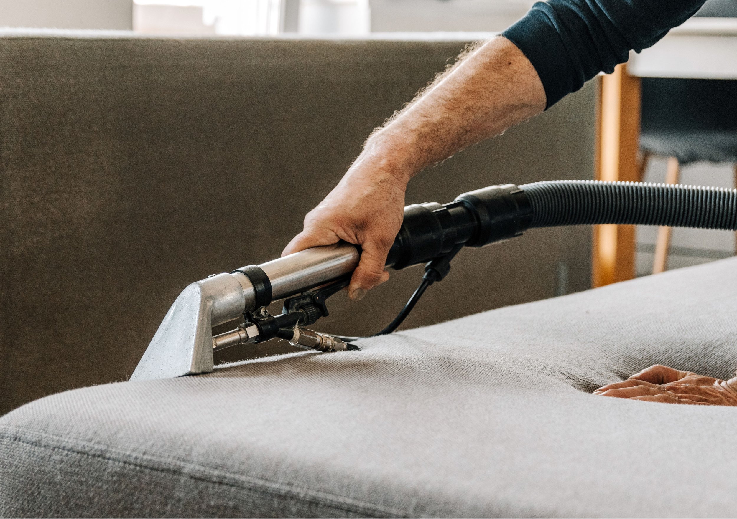 A person using a vacuum cleaner to clean a light gray sofa.