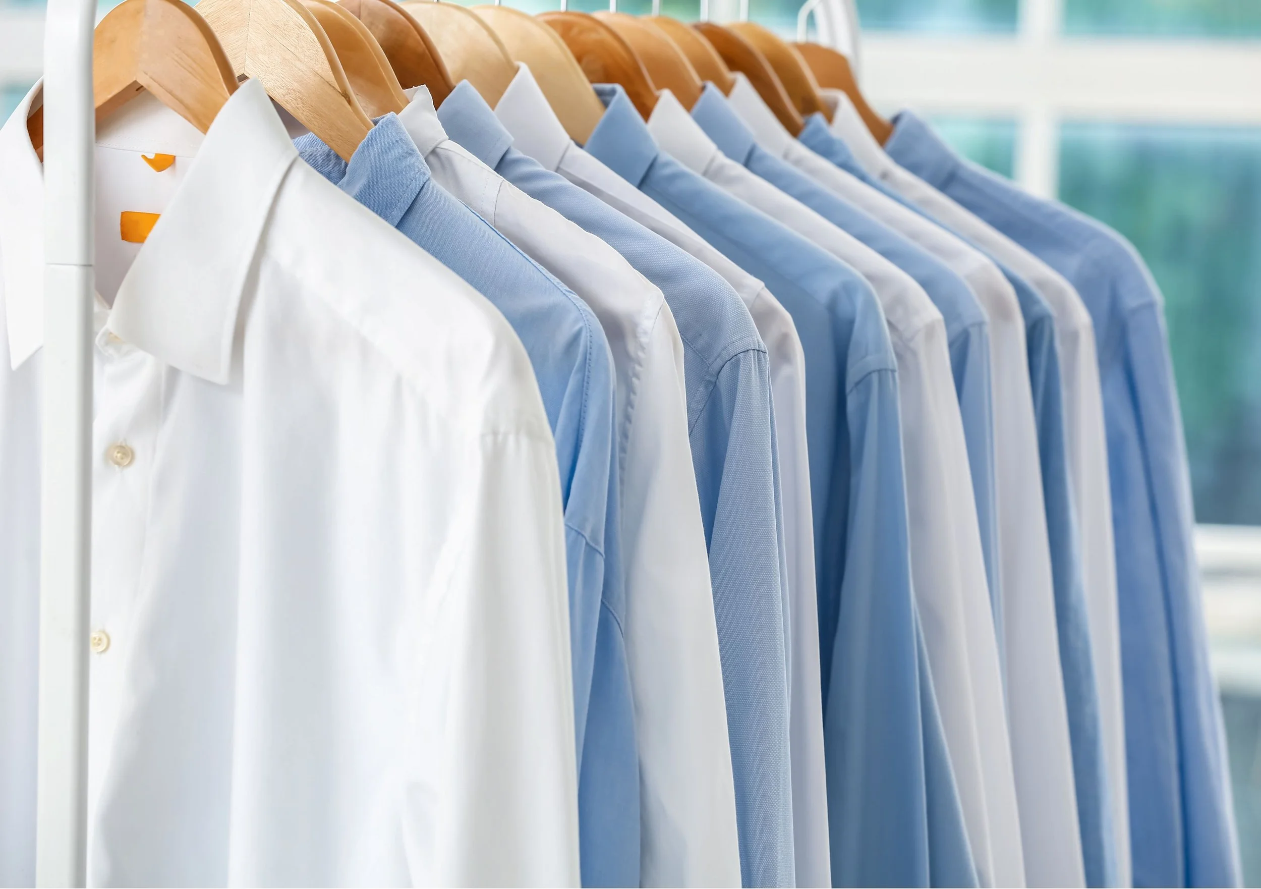 A row of washed and ironed shirts hanging on wooden hangers on a white clothing rack.